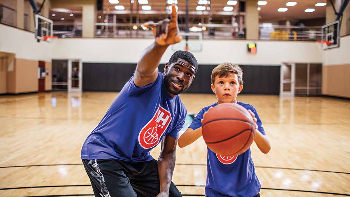 Image of a basketball coach teaching a boy to shoot a basket