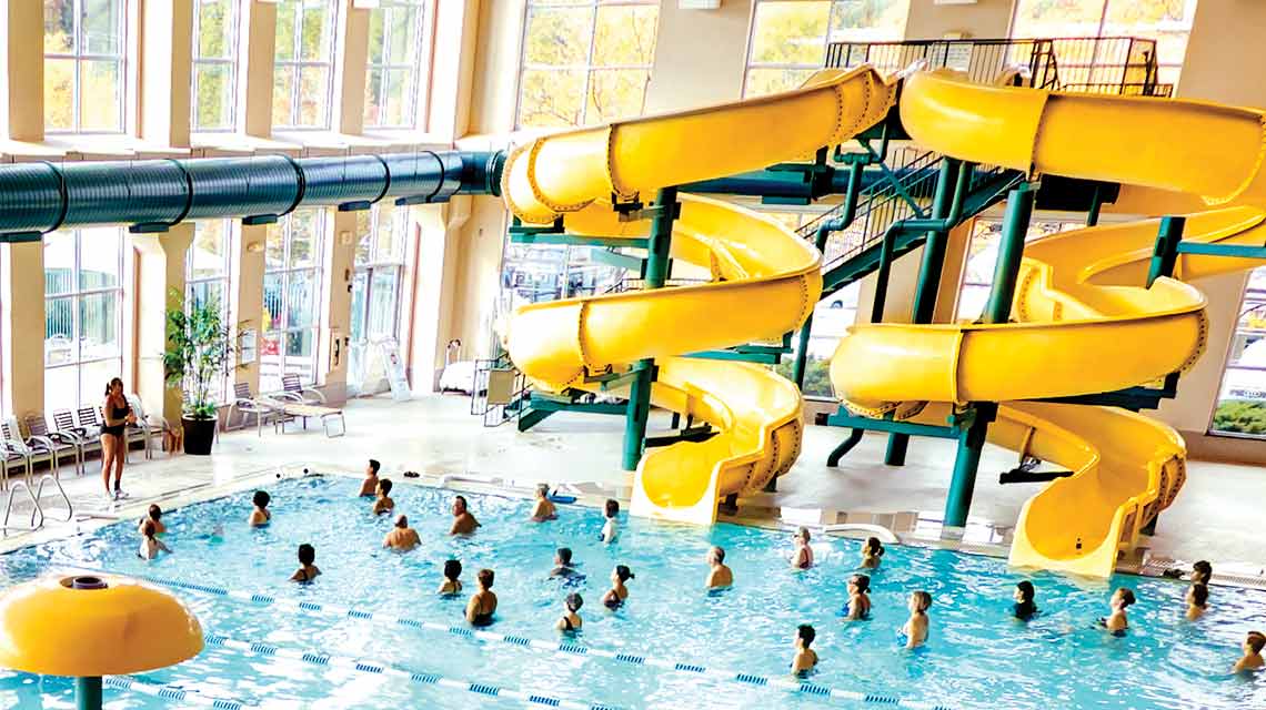 An aerial view of an expansive indoor pool with two curving yellow waterslides