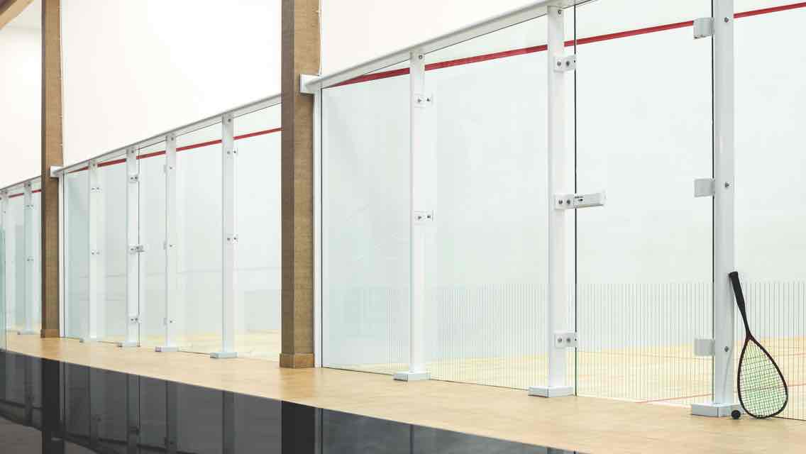A line of glass-enclosed squash courts behind a reception desk with a sign reading “Life Time Squash”