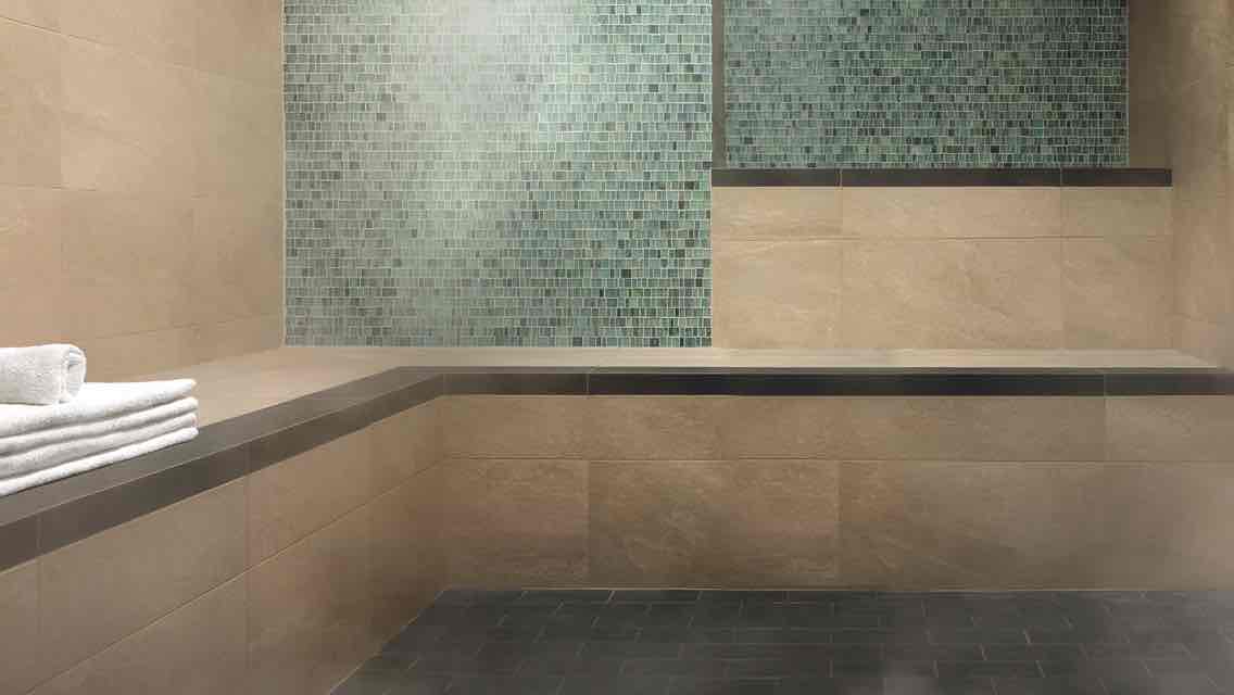 A luxurious, tile-lined steam room with a stack of white towels at the ready