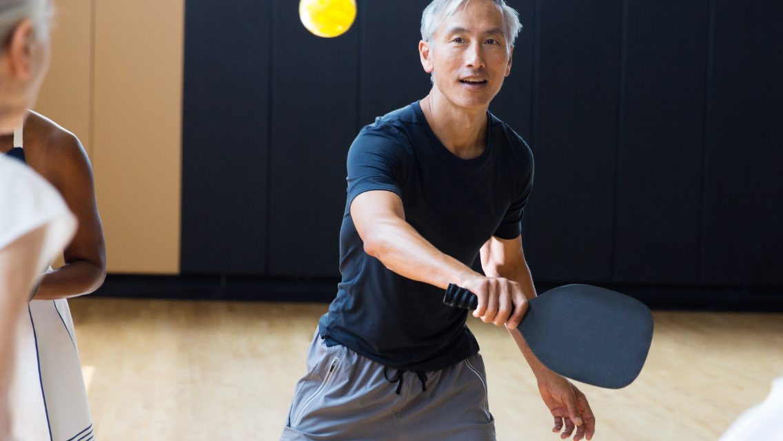 Man in black shirt playing pickleball in a gym
