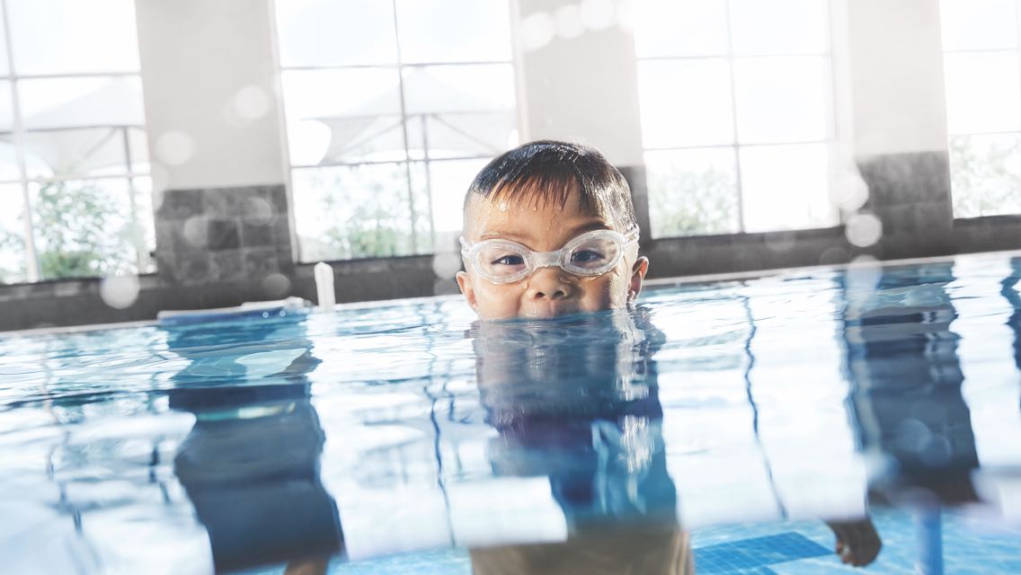 A child wearing swim goggles sticking his head up from underwater