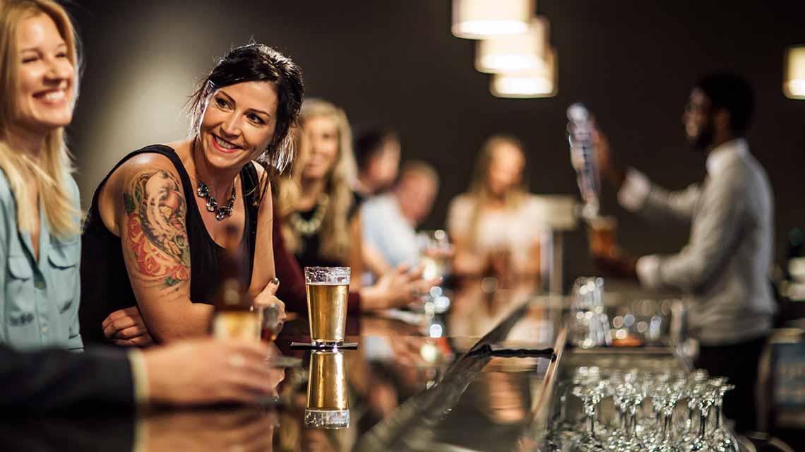a bartender serves a group of smiling, happy, people at a bar counter